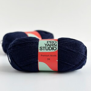 K&ouml;nnte beinhalten: Zwei Kn&auml;uel marineblaues Garn mit einem roten und wei&szlig;en Etikett mit der Aufschrift "Pro Yarn Studio" und "Premium Acrylic DK".