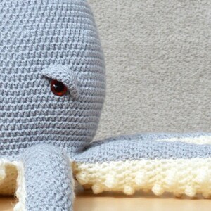 May include: A gray crocheted octopus with a white crocheted trim on the tentacles. The octopus has one red eye.