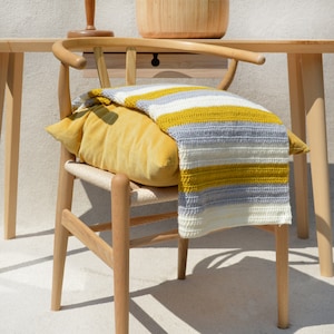 May include: A wooden chair with a yellow and gray striped throw blanket draped over the back. The chair has a woven seat and a natural wood finish.