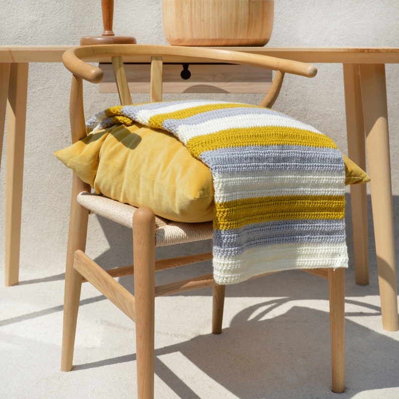 May include: A wooden chair with a yellow and gray striped throw blanket draped over the back. The chair has a woven seat and a natural wood finish.