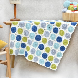 May include: A crocheted blanket with a white background and a pattern of blue, green, and gray circles.