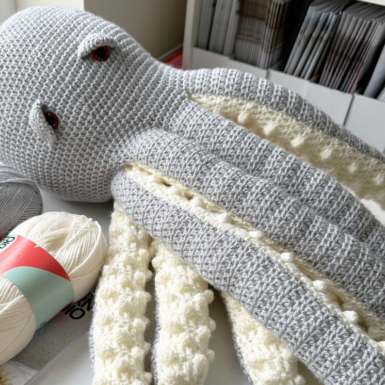May include: A gray crocheted octopus with white crocheted tentacles. The tentacles have a textured, bumpy surface.