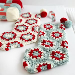 May include: Two handmade Christmas stockings in a granny square pattern. One is off-white with red and light blue accents, the other is light blue with red and white accents. Each stocking has a matching pom-pom. Yarn skeins are visible in the background.