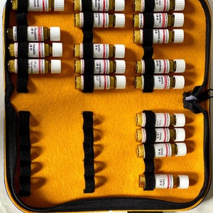 Könnte beinhalten: Ein gelbes Filzetui mit schwarzem Reißverschluss, das mehrere kleine Glasfläschchen enthält. Die Fläschchen werden von schwarzen Gummibändern gehalten. Der Text ist auf Deutsch.