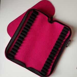 May include: A pink felt pencil case with a zipper closure and black elastic loops for holding pencils. The case has the text "KCD" printed on the side.