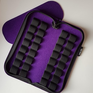 Op de afbeelding: Paarse gevoerde etui met rits en zwarte elastische lussen om kleine spullen in op te bergen. De etui heeft een label met de tekst "100% Wol".