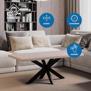 Könnte beinhalten: Ein moderner Couchtisch mit einer hellbraunen Tischplatte und einem schwarzen X-förmigen Gestell. Der Tisch steht in einem Wohnzimmer mit einem weißen Sofa und Kissen.