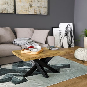 Könnte beinhalten: Ein Holz-Couchtisch mit einem schwarzen X-förmigen Gestell. Der Tisch hat eine helle Holzoptik und ist mit einem Tablett mit Snacks und Getränken dekoriert.