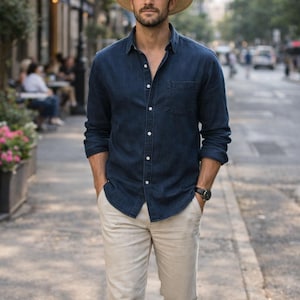 Könnte beinhalten: Ein Mann mit Strohhut, marineblauem Hemd und beiger Hose geht eine Straße entlang. Das Hemd ist geknöpft und hat eine Brusttasche. Er trägt eine schwarze Uhr. Die Szene spielt in einer Stadt.