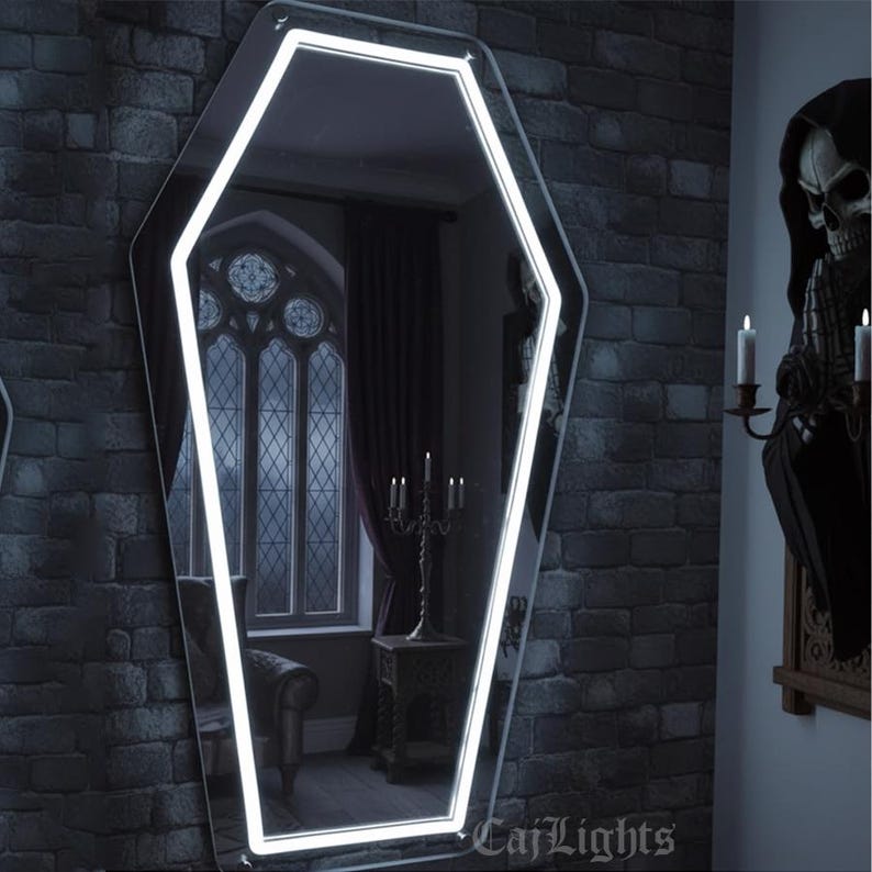 May include: Coffin-shaped mirror with a bright white LED outline, mounted on a dark gray brick wall. The mirror reflects a room with a gothic window, a candelabra, and a decorative table. The mirror is a unique decorative item.