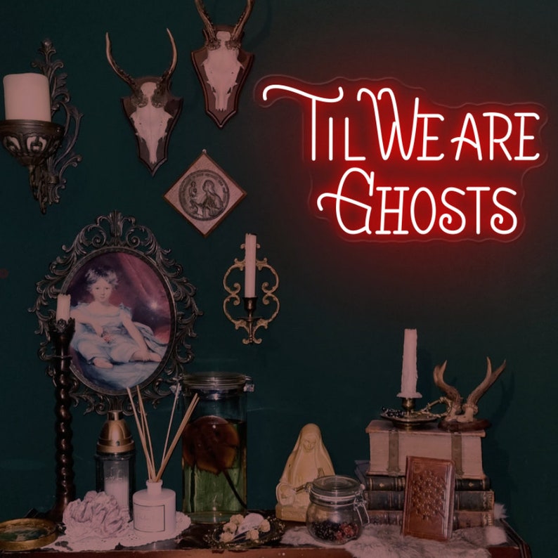 May include: A dark green wall with a neon sign that reads "Til We Are Ghosts". The wall is decorated with antlers, candles, and other decorative items.