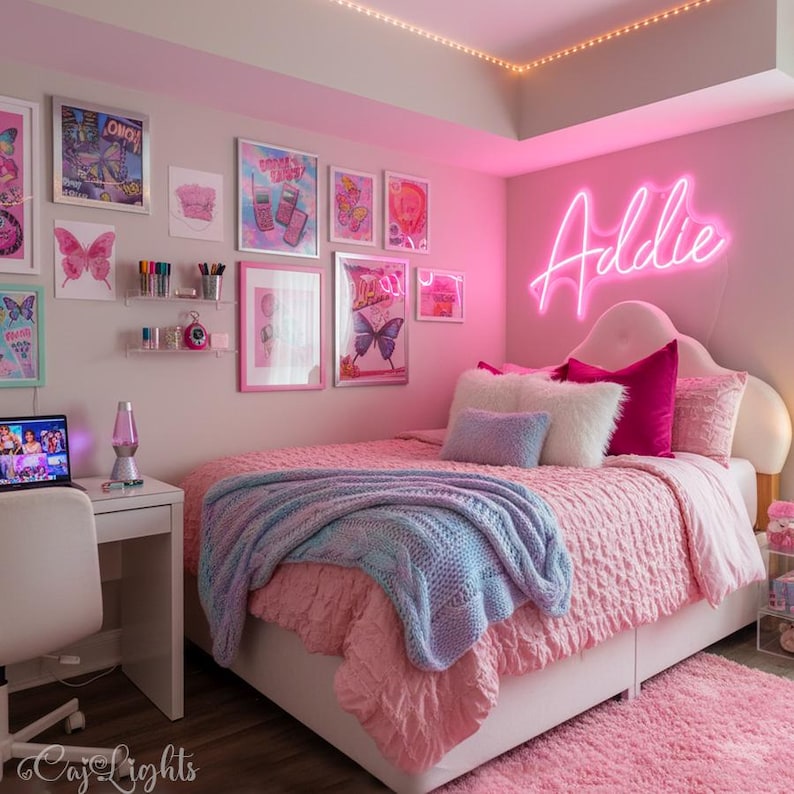 May include: A bedroom featuring a bed with a pink textured comforter, a light blue knit throw blanket, and various pillows. A neon sign on the wall displays the name Addie in pink. The walls are decorated with framed butterfly art and prints.