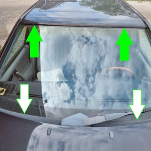 May include: A close-up view of a car's windshield, reflecting a cloudy sky. The dark-colored car has a visible windshield wiper and a brown trim. The image is taken from a high angle, showing the car's hood and roof.