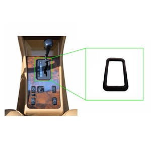 Op de afbeelding: Een zwart, rechthoekig frame voor de versnellingspook van een auto. Het frame wordt op een witte achtergrond getoond. De afbeelding toont ook de versnellingspook van de auto en de omliggende console met houtnerf.