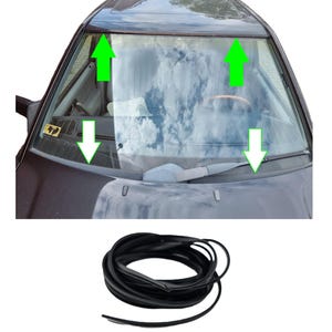 May include: A black rubber windshield seal coiled at the bottom of the image, with a car windshield in the background. The windshield has green arrows pointing to the seal's placement. The car's interior is visible through the glass, with a steering wheel.