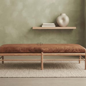 May include: A rectangular bench featuring a brown leather upholstered seat cushion supported by a light-toned wooden frame with cylindrical legs and horizontal support bars connecting the base structure.