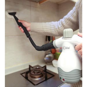 Può includere: Un pulitore a vapore portatile bianco e grigio con un ugello nero viene utilizzato per pulire una parete della cucina. Il pulitore a vapore ha il marchio "Kiwi" stampato sopra. L'apparecchio viene utilizzato vicino a un fornello.