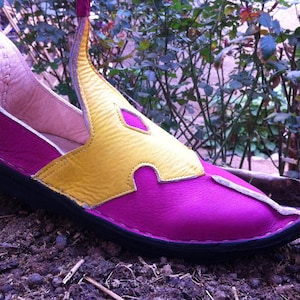 May include: A pointed-toe shoe featuring a vibrant magenta leather base with a contrasting yellow leather overlay on the upper. The shoe has a black sole, visible stitching along the edges, and a high, curved heel collar with a distinct, elongated shape.