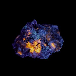 Pode incluir: Close-up de uma formação rochosa sobre um fundo preto. A rocha apresenta uma mistura de cores azul, laranja e verde. As áreas laranja parecem brilhar, e a textura é áspera e irregular.