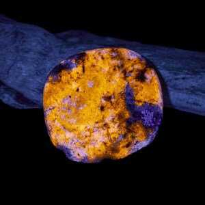 May include: A glowing, rounded stone with a vibrant color palette. The stone features a mix of bright yellow, orange, and deep purple hues, creating a striking contrast. The surface has a textured appearance, with darker spots and patterns.