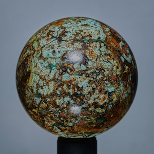 May include: A spherical decorative object with a mottled surface. The sphere features a mix of turquoise, brown, and gold colors, creating a unique, textured appearance. The object is mounted on a black base.