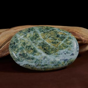 Pode incluir: Uma pedra polida em forma oval com um padrão manchado de verde, amarelo e branco. A pedra tem uma superfície lisa e brilhante e parece ser um espécime mineral natural. A pedra tem aproximadamente 10 cm de diâmetro.