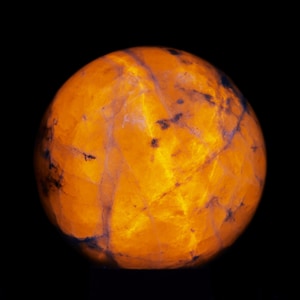 May include: A glowing, spherical gemstone with a vibrant orange hue, set against a stark black background. The orb's surface displays intricate patterns and dark veins, creating a textured appearance. The gemstone's internal light gives it a warm, inviting glow.