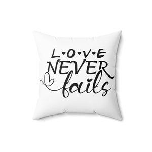 Könnte beinhalten: Ein weißes Kissen mit schwarzem Text, der "L.O.V.E NEVER fails" lautet, mit kleinen Herzen zwischen den Buchstaben und um das Wort "fails".