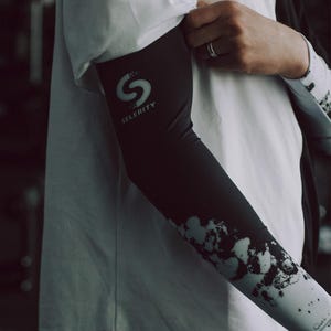 May include: Black and white arm sleeve with the word "SELERITY" and a stylized "S" logo. The sleeve has a white and black abstract design on the lower portion. The person is wearing a white t-shirt.