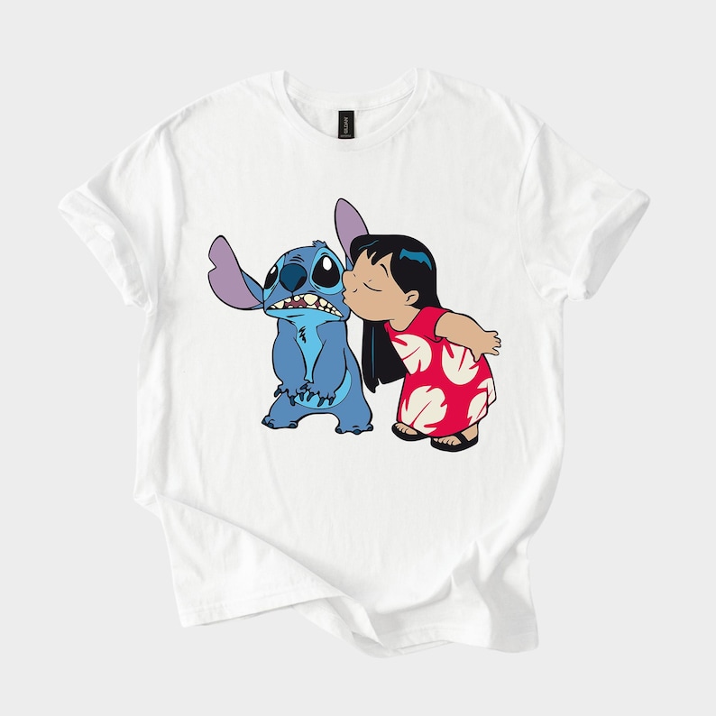 May include: White t-shirt featuring a cartoon illustration of Stitch, a blue alien, being kissed on the cheek by a girl in a red dress. The design is a colorful graphic print, perfect for fans of the animated movie.
