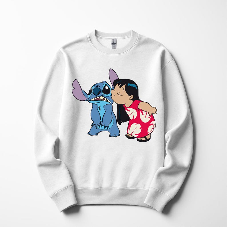 May include: White sweatshirt featuring a graphic of Stitch and Lilo from the Disney movie Lilo & Stitch. Lilo is kissing Stitch on the cheek. Stitch is blue with large ears. Lilo is wearing a red dress with white floral designs.