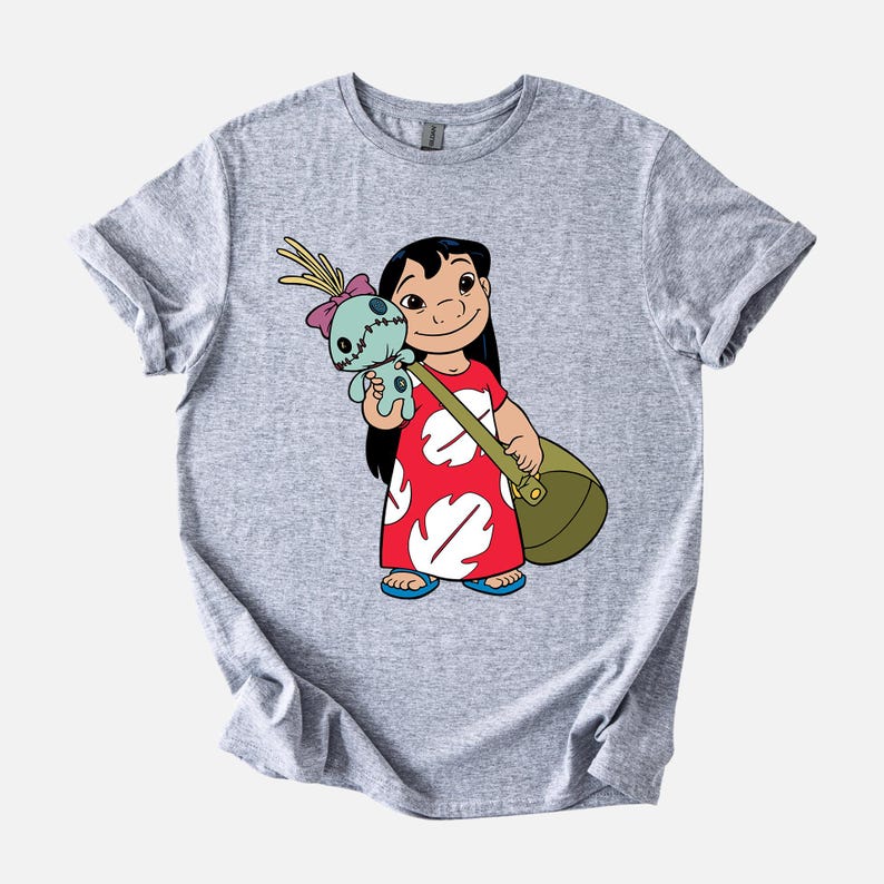 Puede incluir: Una camiseta gris claro con una ilustraci&oacute;n de dibujos animados de una ni&ntilde;a con un vestido rojo con detalles blancos, que lleva una bolsa verde y una mu&ntilde;eca azul. La ni&ntilde;a tiene el pelo negro y sonr&iacute;e. La camiseta tiene mangas enrolladas.