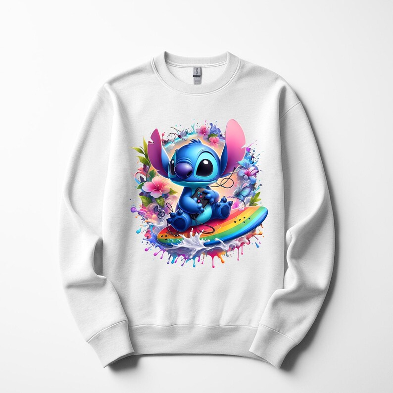 Peut inclure: Sweat-shirt blanc avec un personnage de dessin anim&eacute; bleu sur une planche de surf arc-en-ciel, entour&eacute; de fleurs et d'&eacute;claboussures de peinture. Le personnage a de grandes oreilles. Design ludique et color&eacute;.