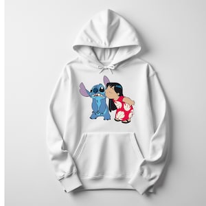 May include: White hooded sweatshirt featuring a graphic of Stitch and Lilo from the Disney movie Lilo & Stitch. Stitch is blue, and Lilo is wearing a red dress with white floral patterns. The design is centered on the front of the sweatshirt.