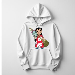 Puede incluir: Sudadera con capucha blanca con una ilustraci&oacute;n de dibujos animados de una ni&ntilde;a con un vestido rojo con formas de hojas blancas, sosteniendo una bolsa verde y una mu&ntilde;eca azul. La ni&ntilde;a tiene el pelo negro y est&aacute; sonriendo. La sudadera tiene un bolsillo delantero.