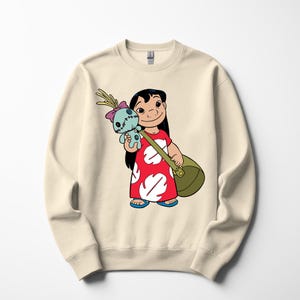 Puede incluir: Sudadera de color crema con una ilustraci&oacute;n de dibujos animados de Lilo Pelekai de la pel&iacute;cula de Disney Lilo & Stitch. Lilo lleva un vestido rojo con dise&ntilde;os blancos y sostiene un mu&ntilde;eco de Stitch y una bolsa verde. La sudadera tiene cuello redondo.