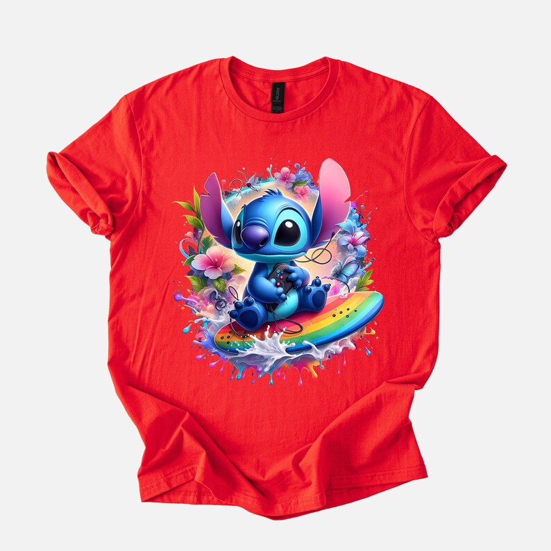 Peut inclure: T-shirt rouge avec un graphisme vibrant d'un personnage de dessin anim&eacute; bleu sur une planche de surf arc-en-ciel, entour&eacute; de fleurs et d'&eacute;claboussures d'eau. Le personnage a de grandes oreilles et tient une manette de jeu.