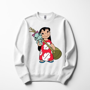 Puede incluir: Sudadera blanca con una ilustraci&oacute;n de dibujos animados de una ni&ntilde;a con un vestido rojo con detalles blancos, sosteniendo una mu&ntilde;eca azul y una bolsa verde. La ni&ntilde;a tiene el pelo negro y est&aacute; sonriendo. La sudadera es de cuello redondo.