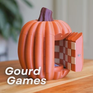 Peut inclure: Un objet orange en forme de citrouille avec une tige brune et une porte articulée qui s'ouvre pour révéler un motif intérieur à damier orange et crème. Le texte Gourd Games est imprimé en blanc sur le côté inférieur gauche de l'image.