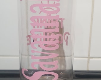 Può includere: Una bottiglia d'acqua in vetro trasparente con fondo in acciaio inossidabile. La bottiglia ha un adesivo in vinile rosa che dice "Stay Happy".