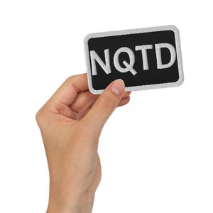 May include: A black patch with white embroidered letters that spell out "NQTD".