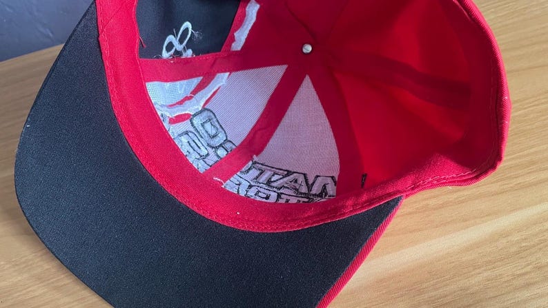K&ouml;nnte beinhalten: Eine rot-schwarze Baseballkappe mit wei&szlig;em Text im Inneren. Die Kappe hat einen schwarzen Schirm und ein rotes Innenfutter. Im Inneren befinden sich wei&szlig;er Text und ein wei&szlig;es Mesh-Futter. Die Kappe ist aus strapazierf&auml;higem Stoff gefertigt.