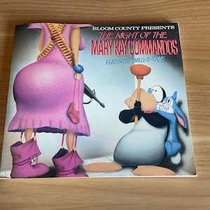 May include: A book cover featuring cartoon characters and the title "THE NIGHT OF THE MARY KAY COMMANDOS". The cover art includes a woman in a pink dress with a machine gun and a cartoon penguin and rabbit.