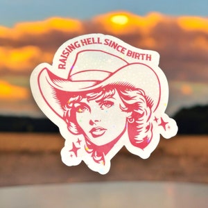 May include: A sticker featuring a red illustration of a woman wearing a cowboy hat. The text "RAISING HELL SINCE BIRTH" is arched above the hat. The sticker has a glittery, holographic effect, with stars and sparkles around the woman's face.