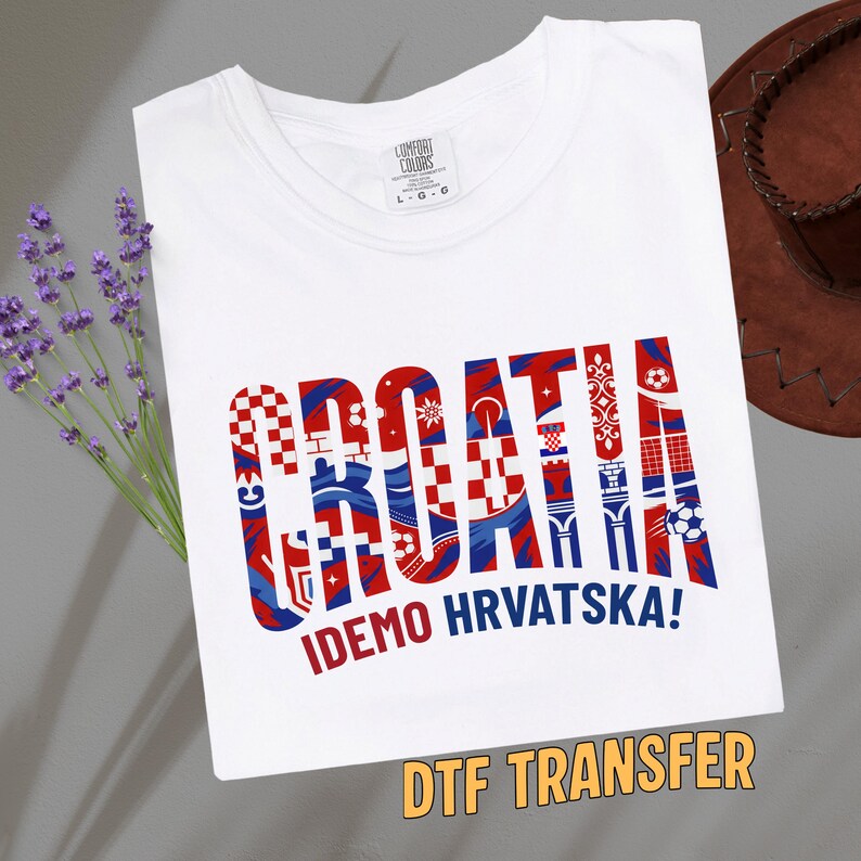 May include: White t-shirt with a large, colorful graphic that says "CROATIA" in red, white, and blue, with the text "IDEMO HRVATSKA!" below. The shirt has a crew neck and short sleeves. The words "DTF TRANSFER" are at the bottom.