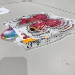 May include: A stack of transparent stickers featuring a pink bow and pencil design with the text "Teaching is a passion". Other stickers include a rainbow design and the words "I teach all".