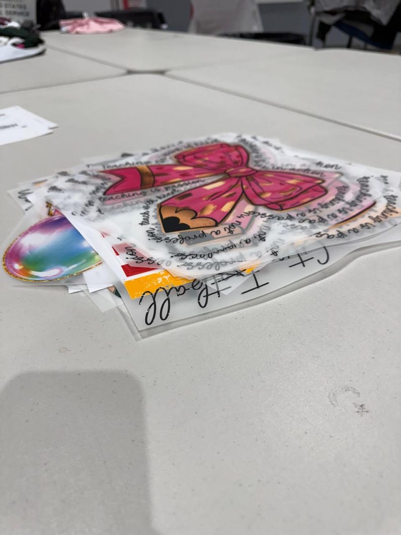 May include: A stack of transparent stickers featuring a pink bow and pencil design with the text "Teaching is a passion". Other stickers include a rainbow design and the words "I teach all".