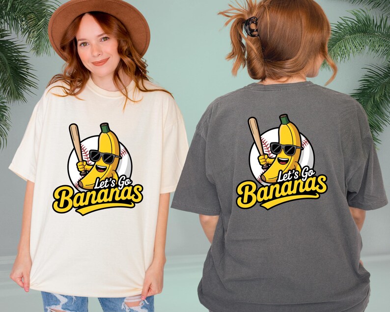 May include: Cream-colored and charcoal gray t-shirts featuring a cartoon banana wearing sunglasses and holding a baseball bat. The text "Let's Go Bananas" is below the banana graphic. The shirts are casual and unisex.