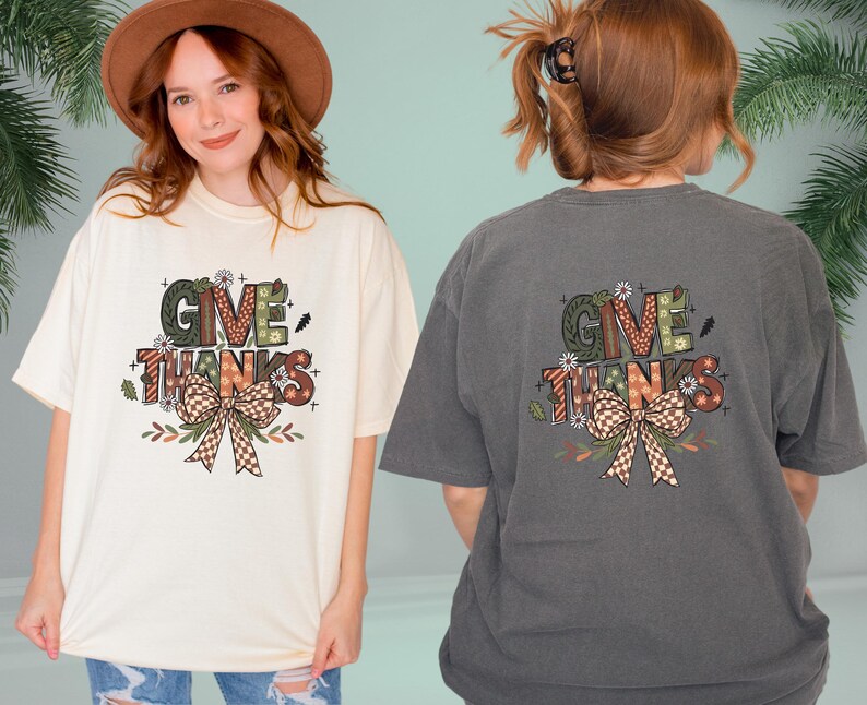 May include: Cream-colored and charcoal gray t-shirts with a graphic that says "GIVE THANKS". The graphic includes a bow, flowers, and fall colors. The shirts are oversized and casual.