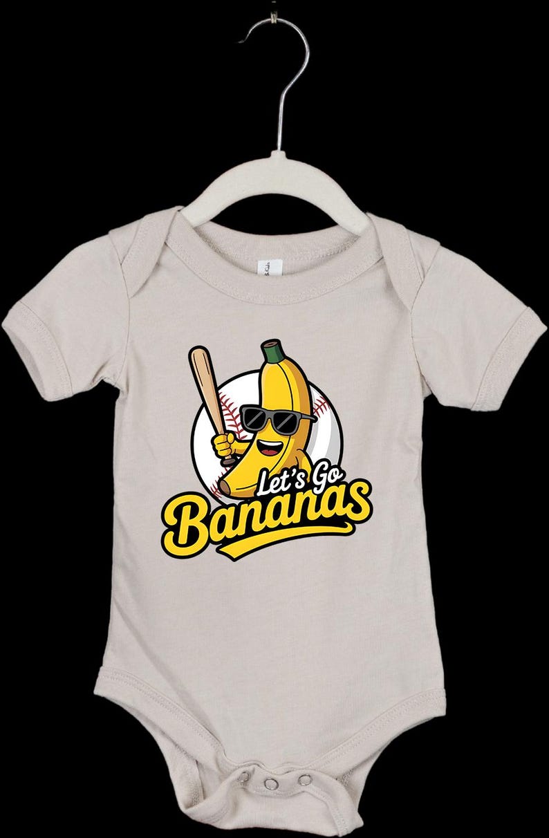 May include: A beige baby onesie with a cartoon banana wearing sunglasses and holding a baseball bat. The design includes a baseball and the text "Let's Go Bananas" in yellow and black.